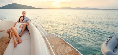 Young couple relaxing on the silicone material seating on the back of their boat with the sunset in the background and a yacht tender floating nearby